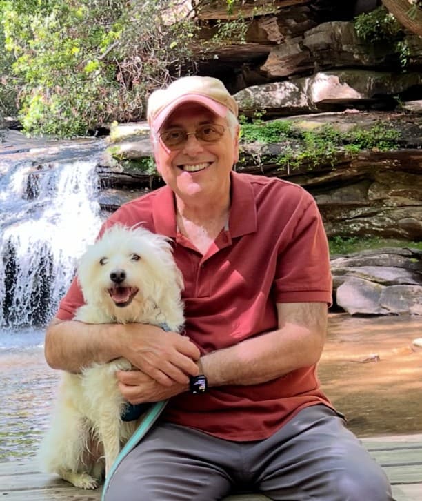 Bernard Robin smiling, holding his dog in front of a waterfall.