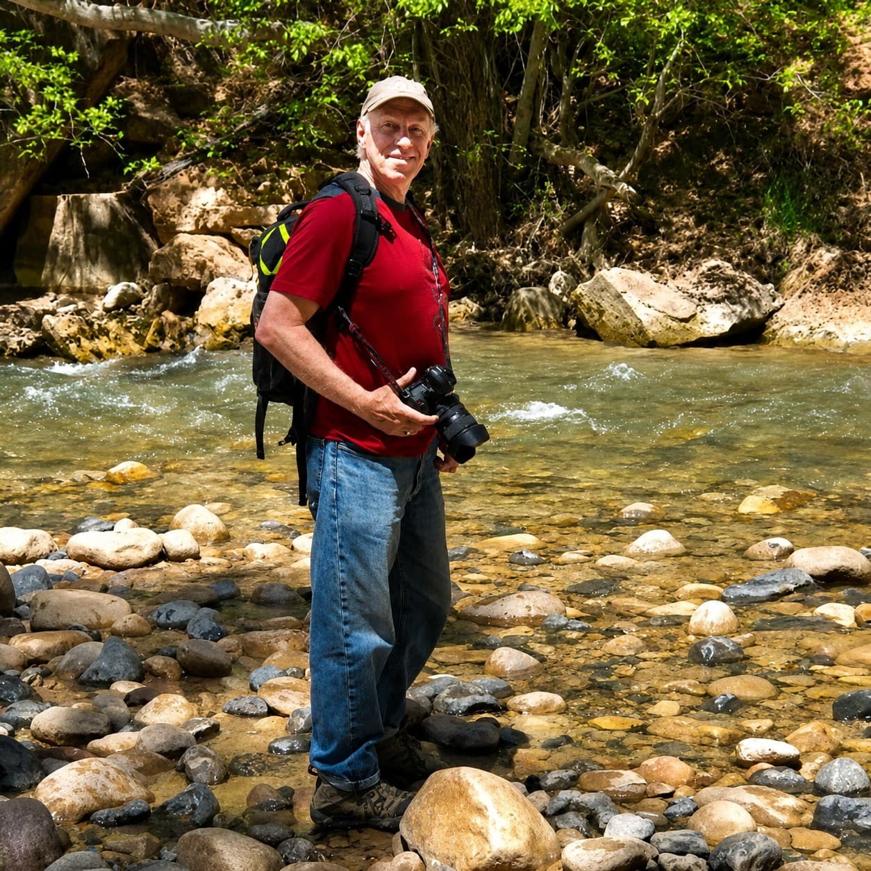 David Schutzman standing in a rocky streambed, holding a camera.